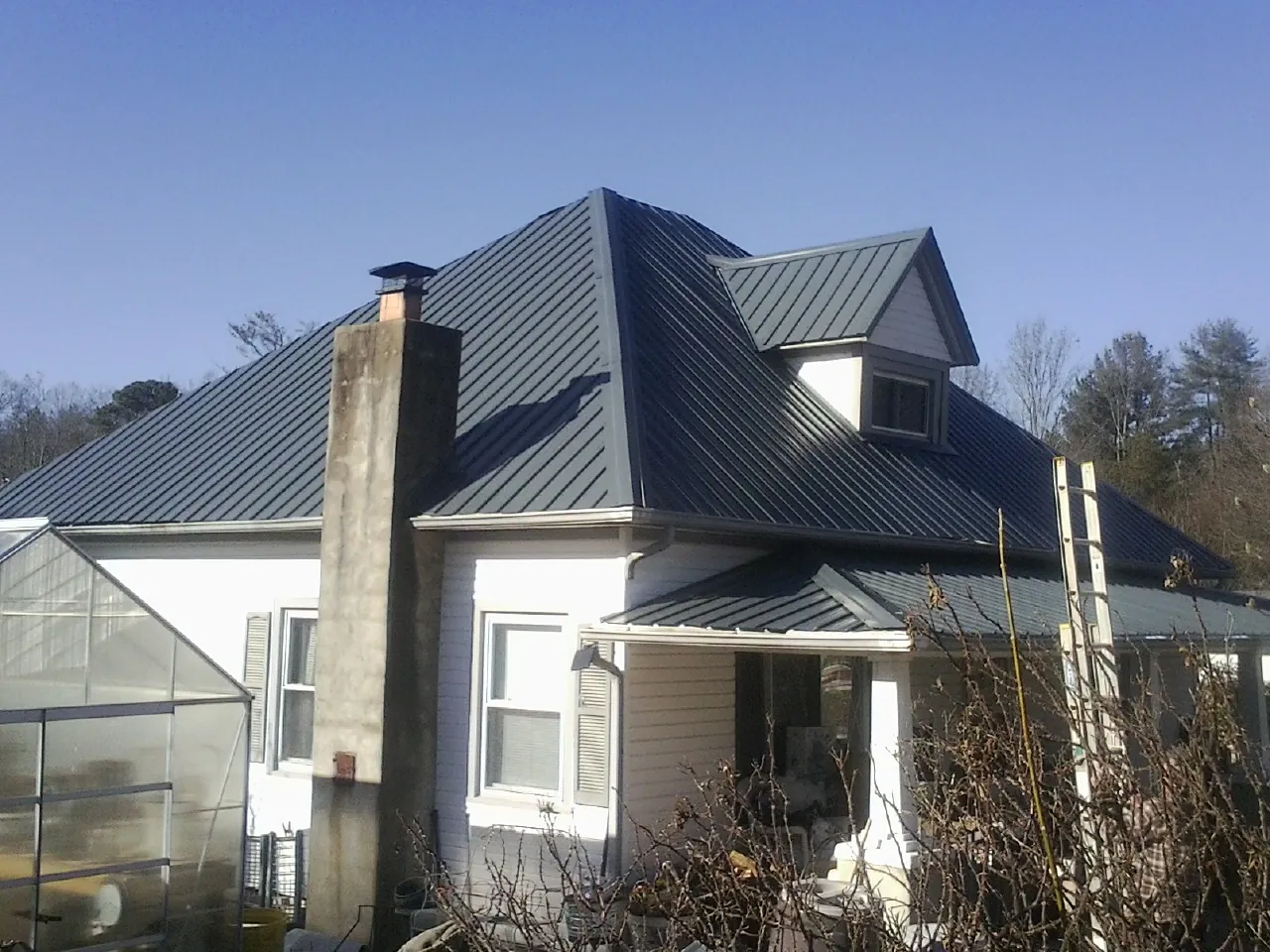 Dark blue standing seam metal roof on a white farmhouse with dormer — Slate & Tile Roof Repair by Roofing Brothers in Robards