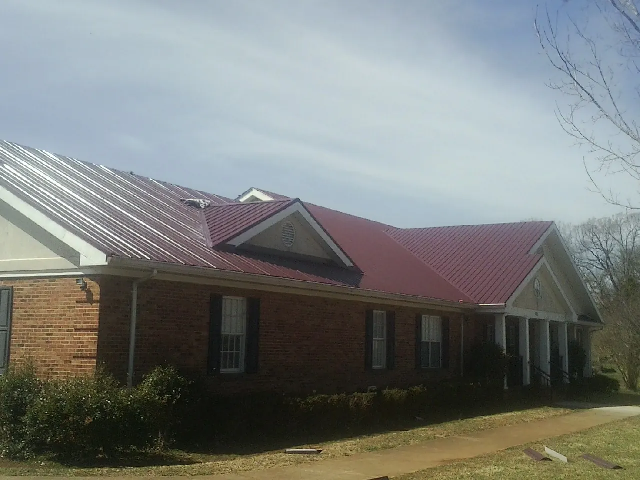 Red metal roof with gabled entries on a long brick building, from a Hail Damage Roof Repair job in Robards