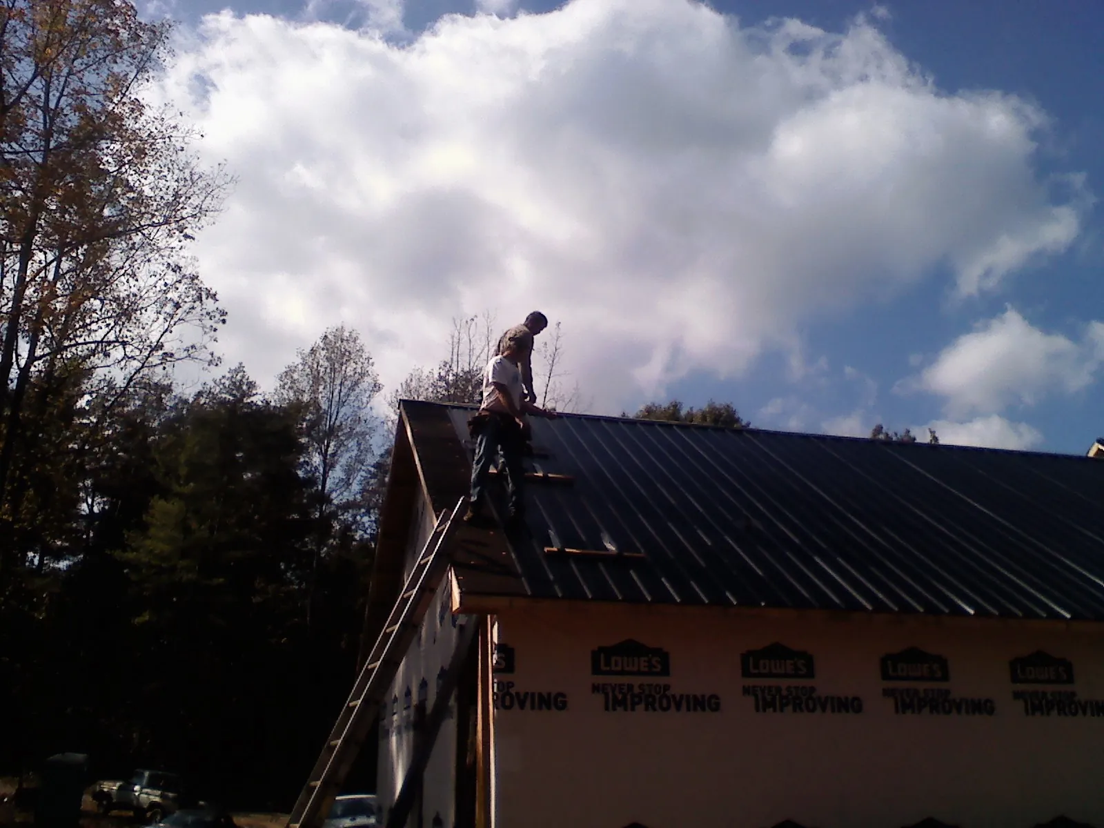 Roofer fastening dark metal panels high against a cloudy sky, from a Roof Inspection job in Robards